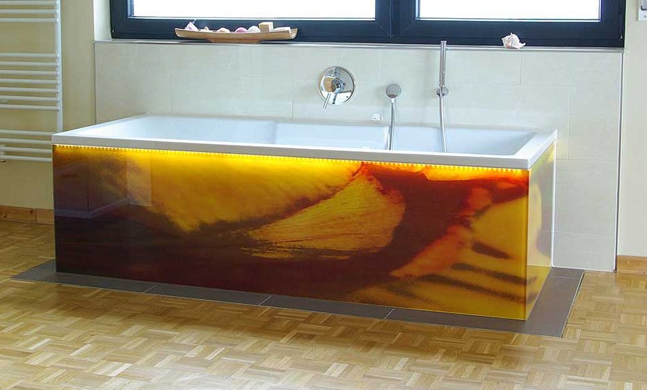 Freestanding bathtub with a glass base and atmospheric LED lighting below the tub rim. The glass surfaces are made of printed safety glass. Recording at daylight.