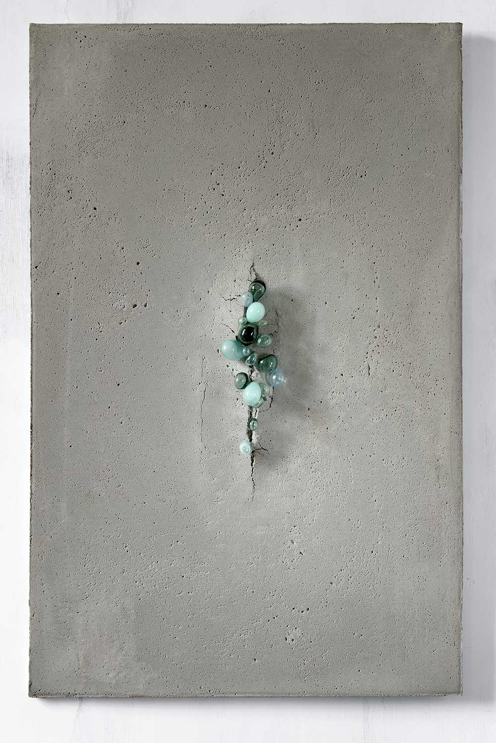 A wall art piece. Various bubbles of molten colored glass penetrate the concrete slab, tear open the slab in the middle and push forward through the concrete layer.