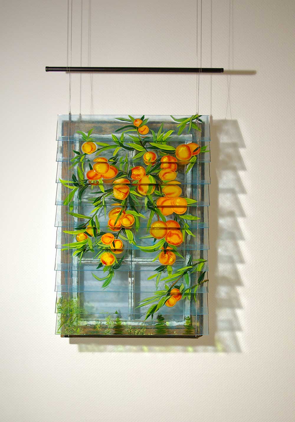 In front of an old wooden window, mounted on the wall, there is a blind made of colored melted glass. The glass slats show peach fruits and branches of a tree. Front view