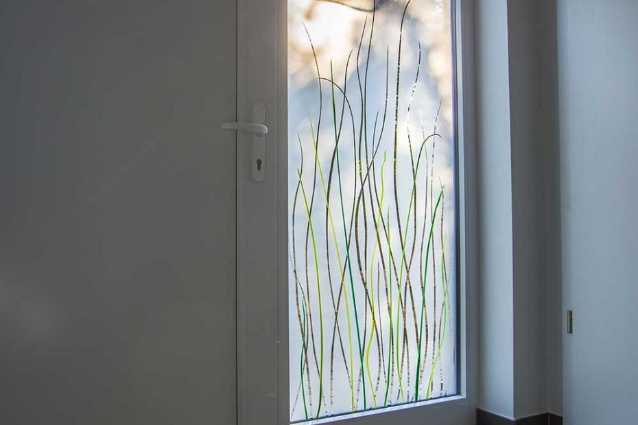 Das Seitenfeld neben der Eingangstüre ist mit einem Design aus grünen, geschmolzenen Farbglas- Gräsern im Scheibenzwischenraum auf einem mattierten Glas gestaltet. Modernes Design unter Berücksichtigung der Wärmedämmung.
