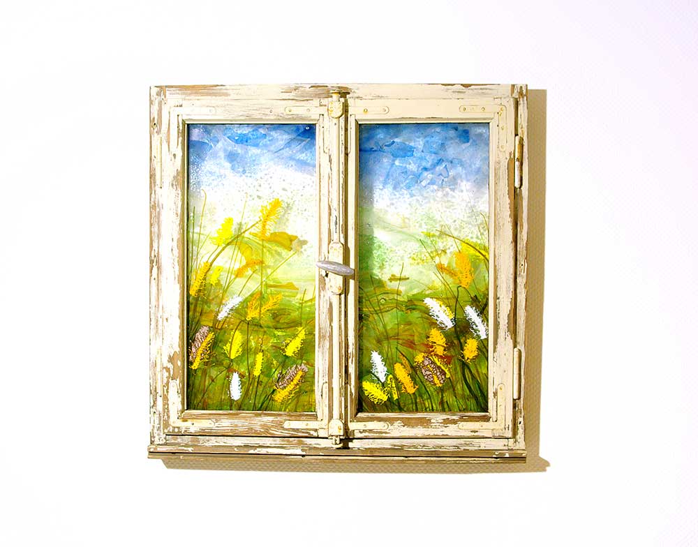 Ein künstlerisch gestaltetes, geschlossenes, altes Holzfenster mit aus farbigem Glas geschmolzenen Pflanzen und Gräsern.
