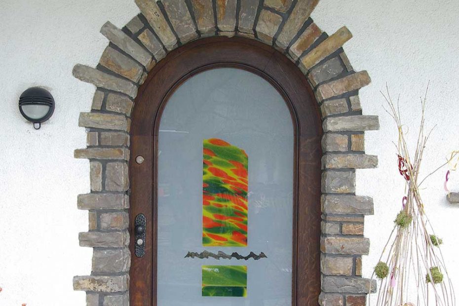 A glass front door with matt sandblasted glass and a laminated blown multiple color flash glass in the center. The colors of the flash glass are orange, yellow and green.