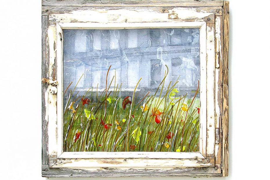 The window is closed and you see the colored melted glass showing a landscape of grasses and meadow flowers.