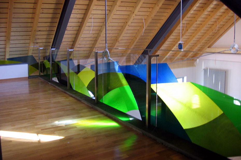 Ein Brüstungsgeländer in einem Gemeindehaus wird zur Kunst außerhalb der Museen. Es besteht aus Sicherheitsglas mit farbig aufgeklebten Echt-Antikglas. Die Transparenten Farbflächen in grün und blau haben die Form von Hügeln und Himmel