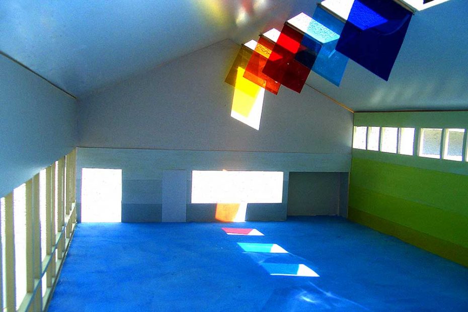 In a model: Transparent panels hang under 5 skylights, form which colored light reflections are shown on one side of the room, throughout the sunlight above a window.