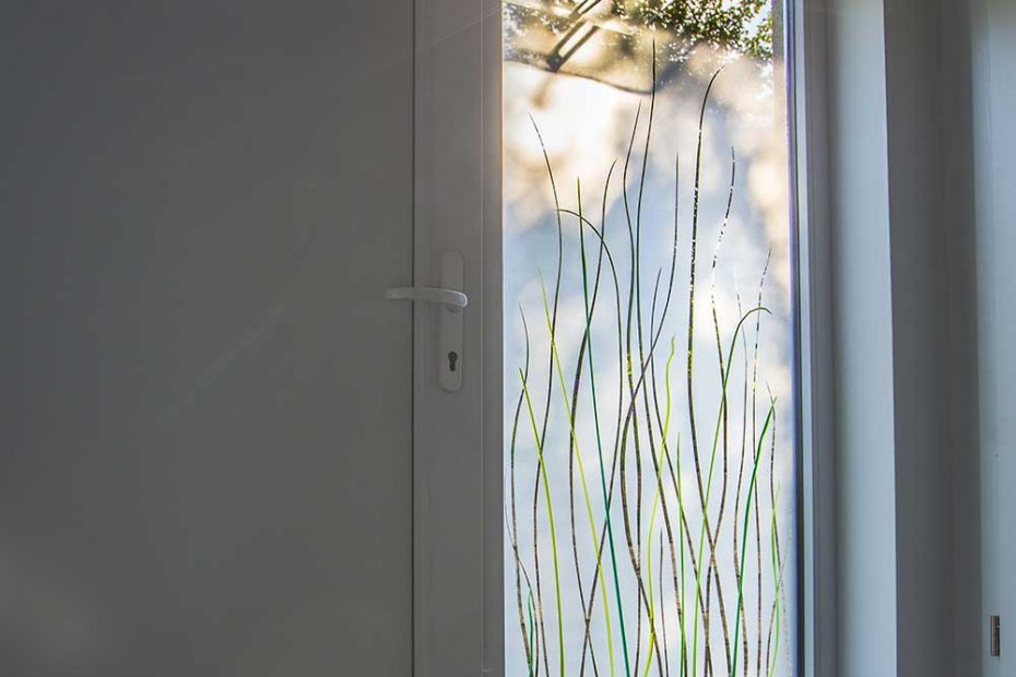 The side panel next to the front door is designed with green, melted colored glass grasses in the space between the panes on a sandblasted, matt glass.