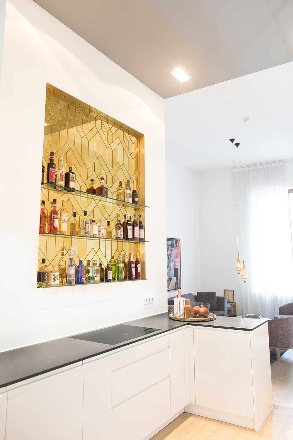An exclusive modern bar with 3 shelves for bottles, consisting of many faced, glued golden antique mirror parts in a brass frame, embedded in the wall.