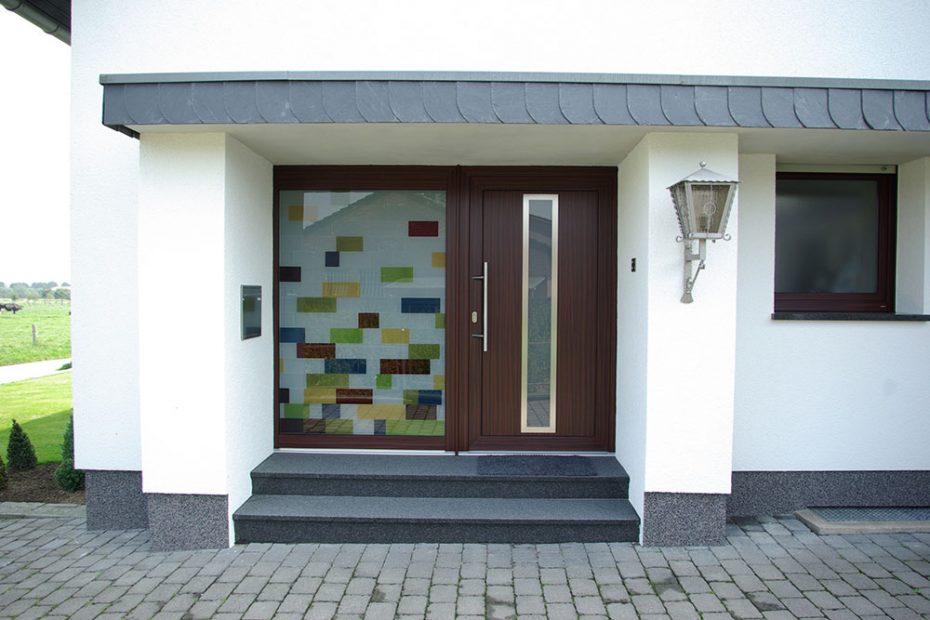 A house entrance door with a side part made from a design of colored rectangles in red, yellow, green and blue, combined with matt glass fields.